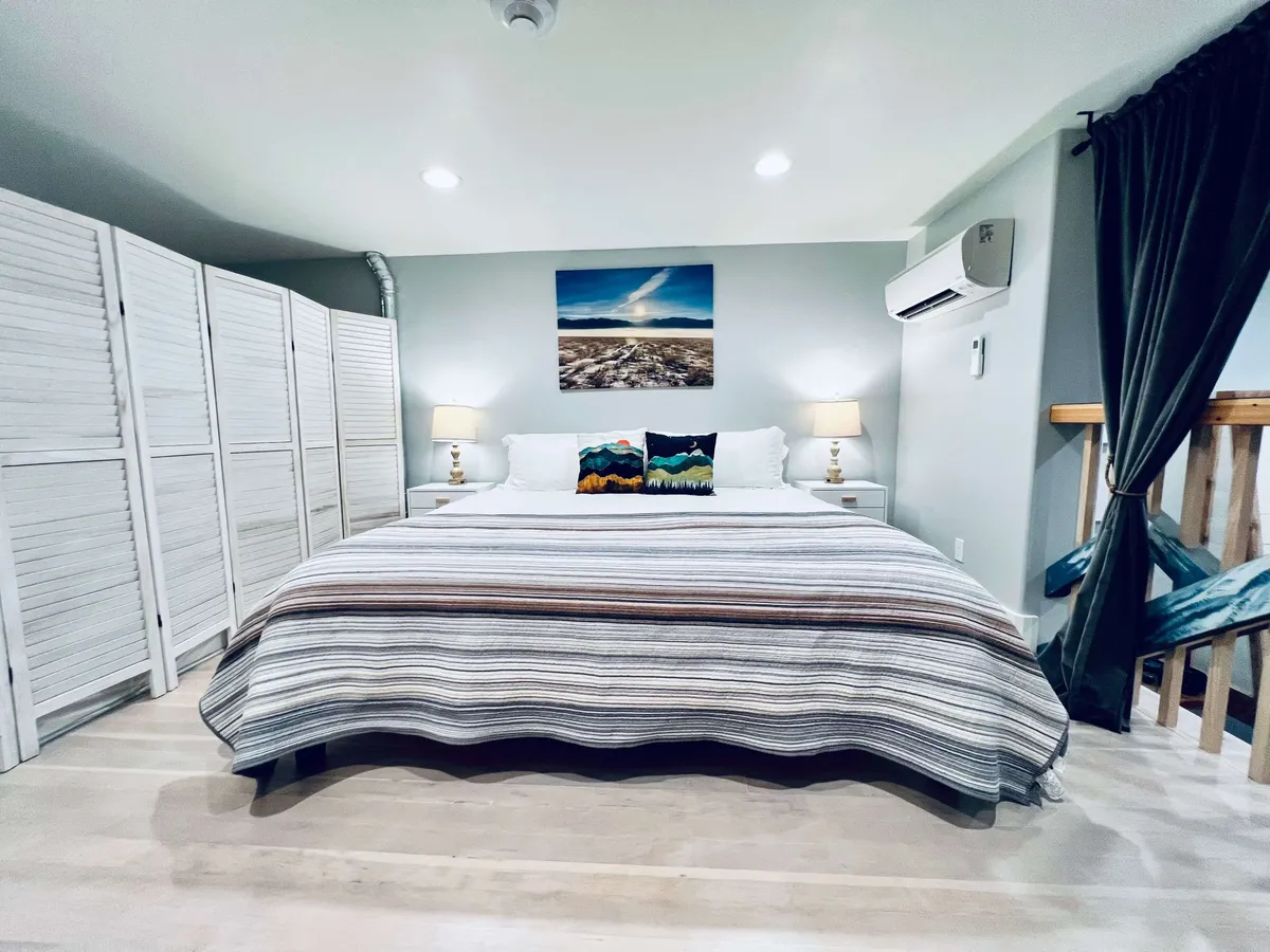This image showcases a spacious bedroom with a large bed adorned with decorative pillows, soft lighting from lamps, and elegant artwork on the wall. Room dividers lend a sense of privacy and coziness, while the overall ambiance is tranquil and inviting—ideal for restful evenings.