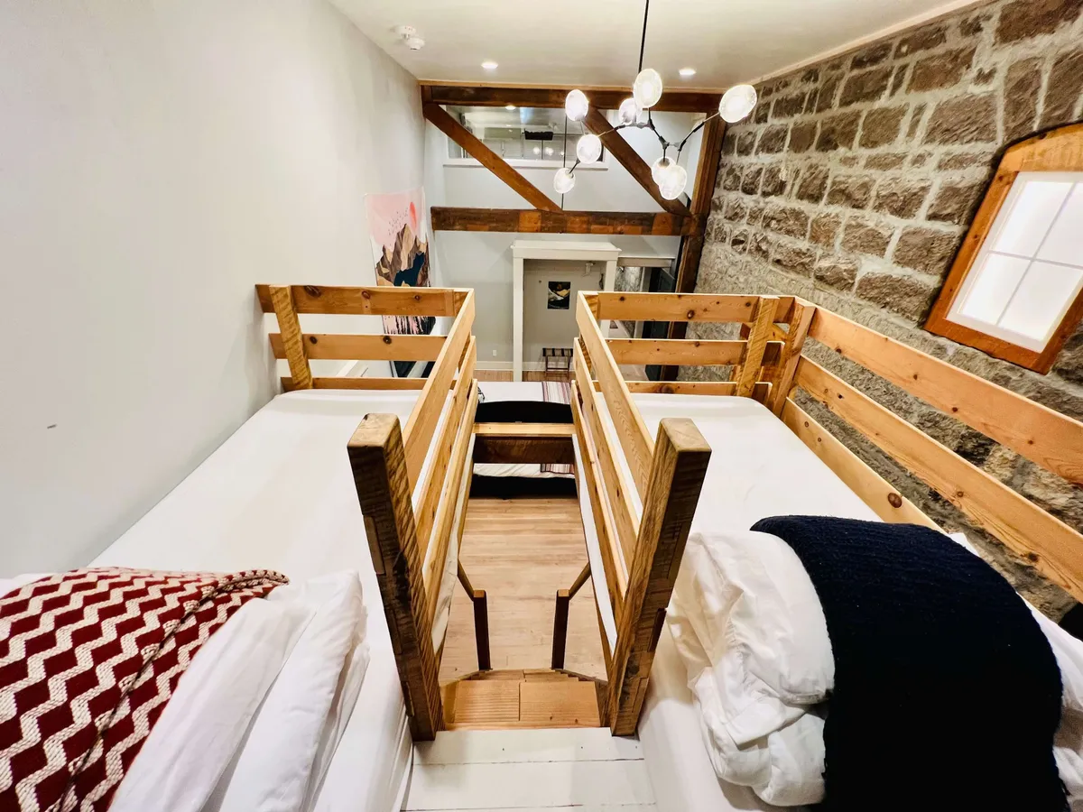 A stylish bedroom features wooden bed frames, exposed stone walls, chandelier lighting, and artistic elements. The space feels both modern and cozy, suggesting a unique and inviting sleeping area ideal for memorable stays.