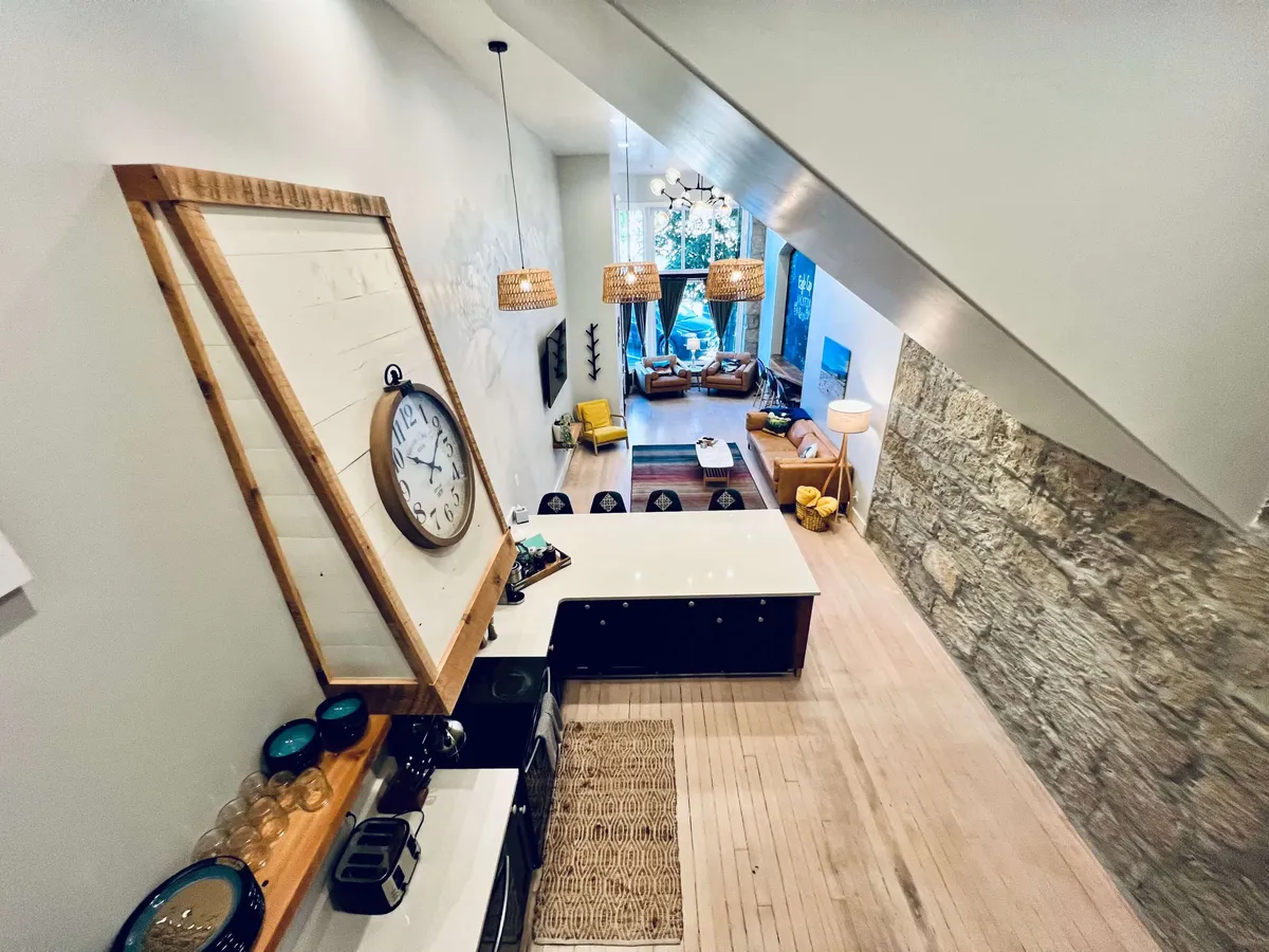 A welcoming living area with a large clock, spacious kitchen island, comfortable seating area, and expansive windows letting in abundant natural light. The arrangement invites relaxation, social gatherings, and casual reading by the window. The decor balances cozy, modern touches with historic elegance.