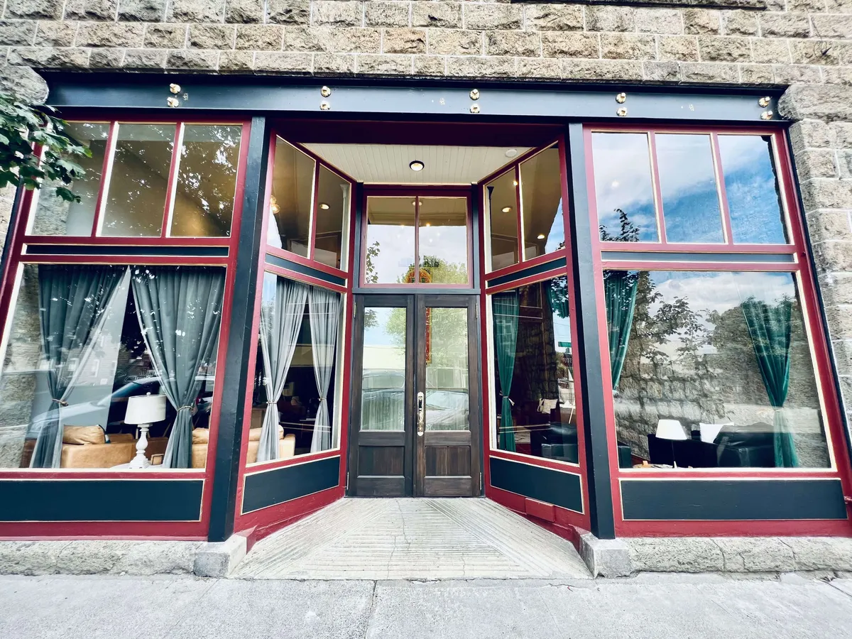 An inviting exterior with large glass windows, a wooden door, and curtains, featuring people enjoying social gatherings, dining, and relaxing. The warm lighting and visible activity hint at both a welcoming atmosphere and the enjoyment of local culture.